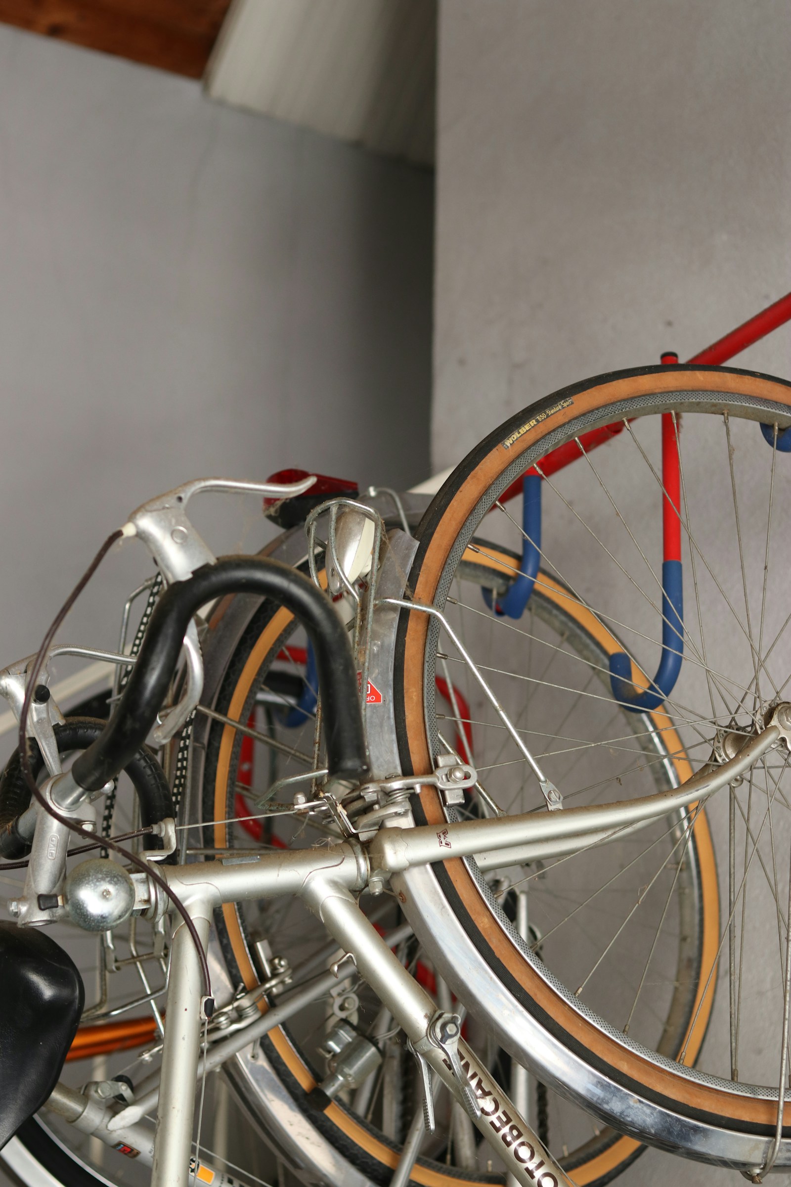 Close-up of bicycles hanging from a red wall-mounted rack beside a gray garage wall