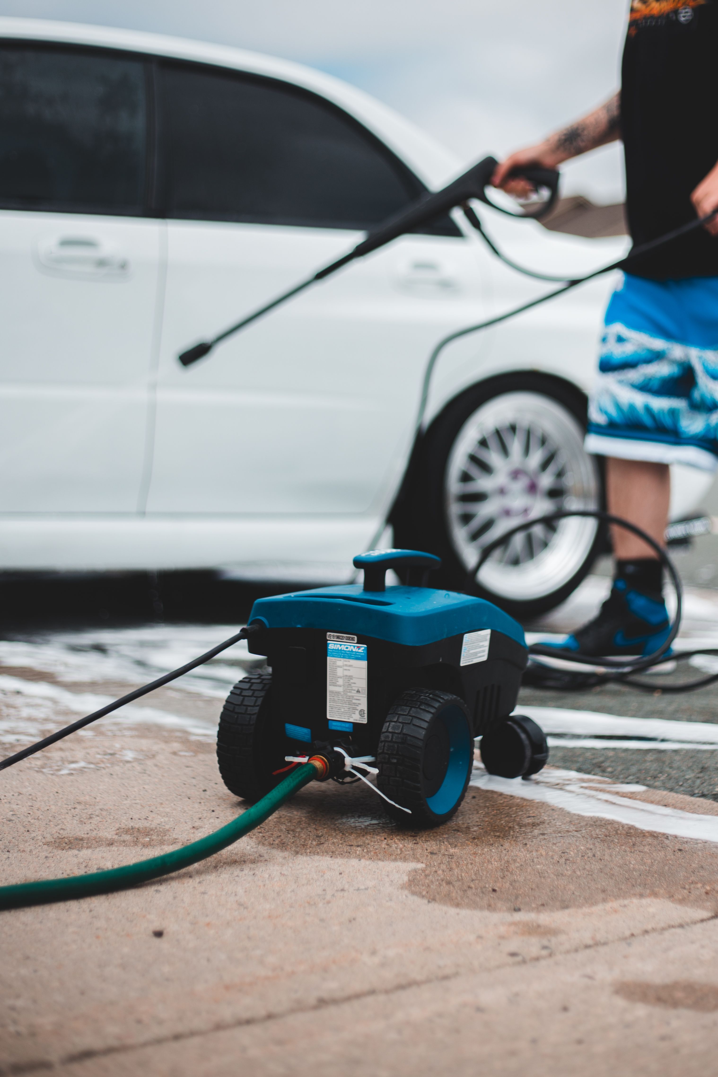 Electric pressure washer with hose and spray wand beside a car